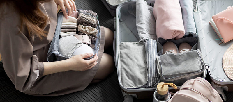A woman sitting on the floor and using packing cubes to organize her suitcase for travel