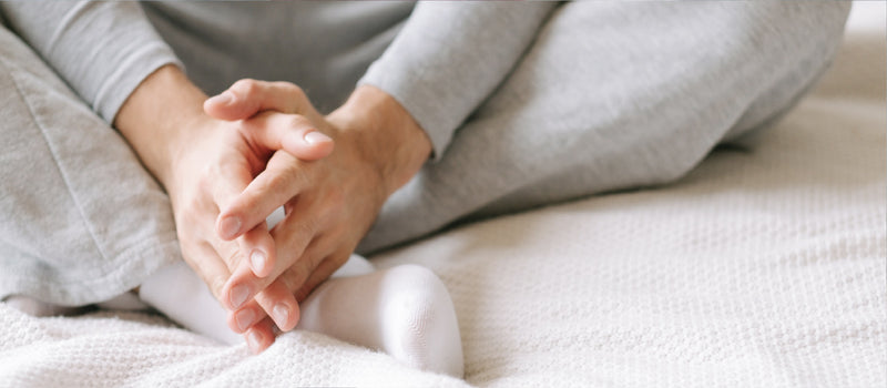 White man wearing grey sweatpants, a grey long sleeve shirt and white socks sitting with his legs crossed and his hands touching